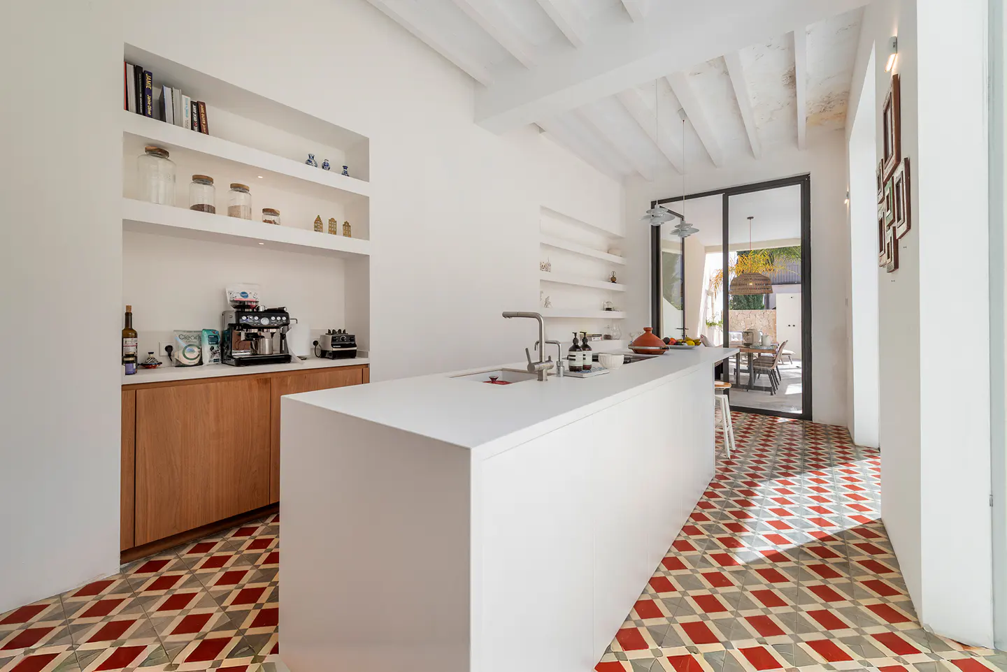 Modern kitchen with white island, wooden cabinets, built-in shelving, and red and white patterned tile flooring.