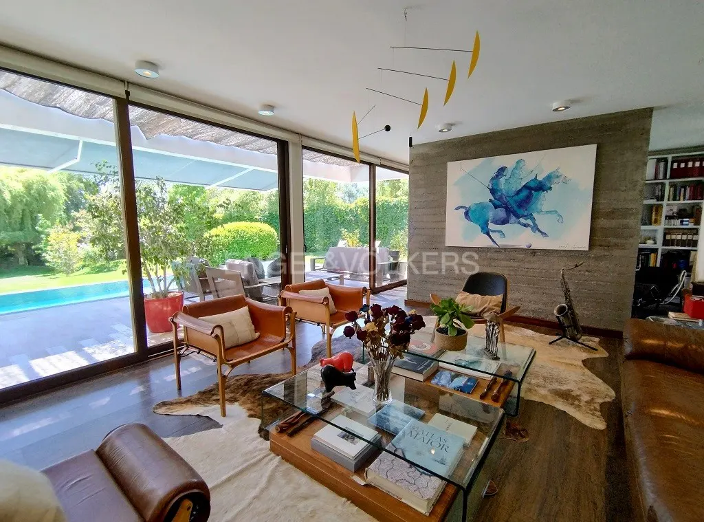 Living room with brown leather furniture, glass coffee table, and a view of a pool and garden through large windows.
