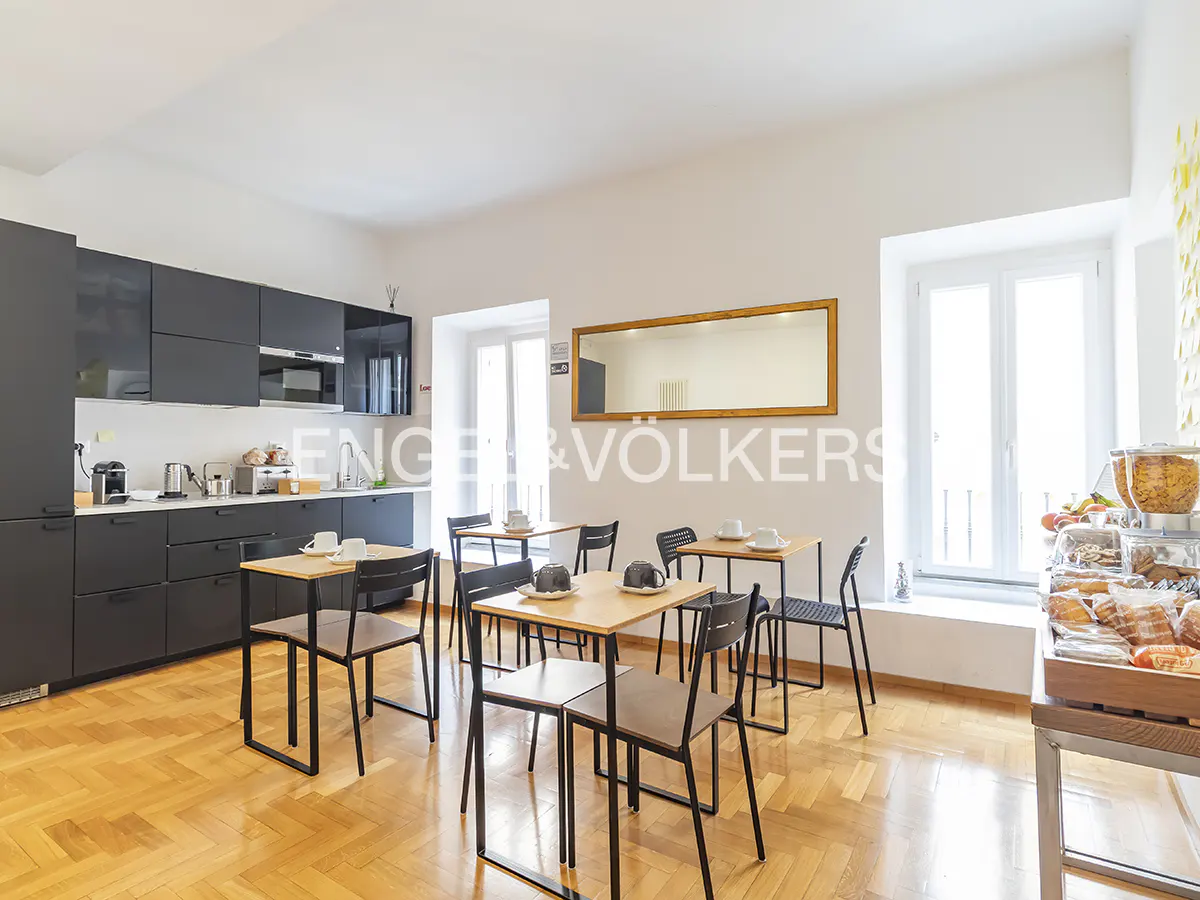 Bright breakfast room with black kitchen cabinets, wood floors, tables with chairs, and a buffet with pastries.