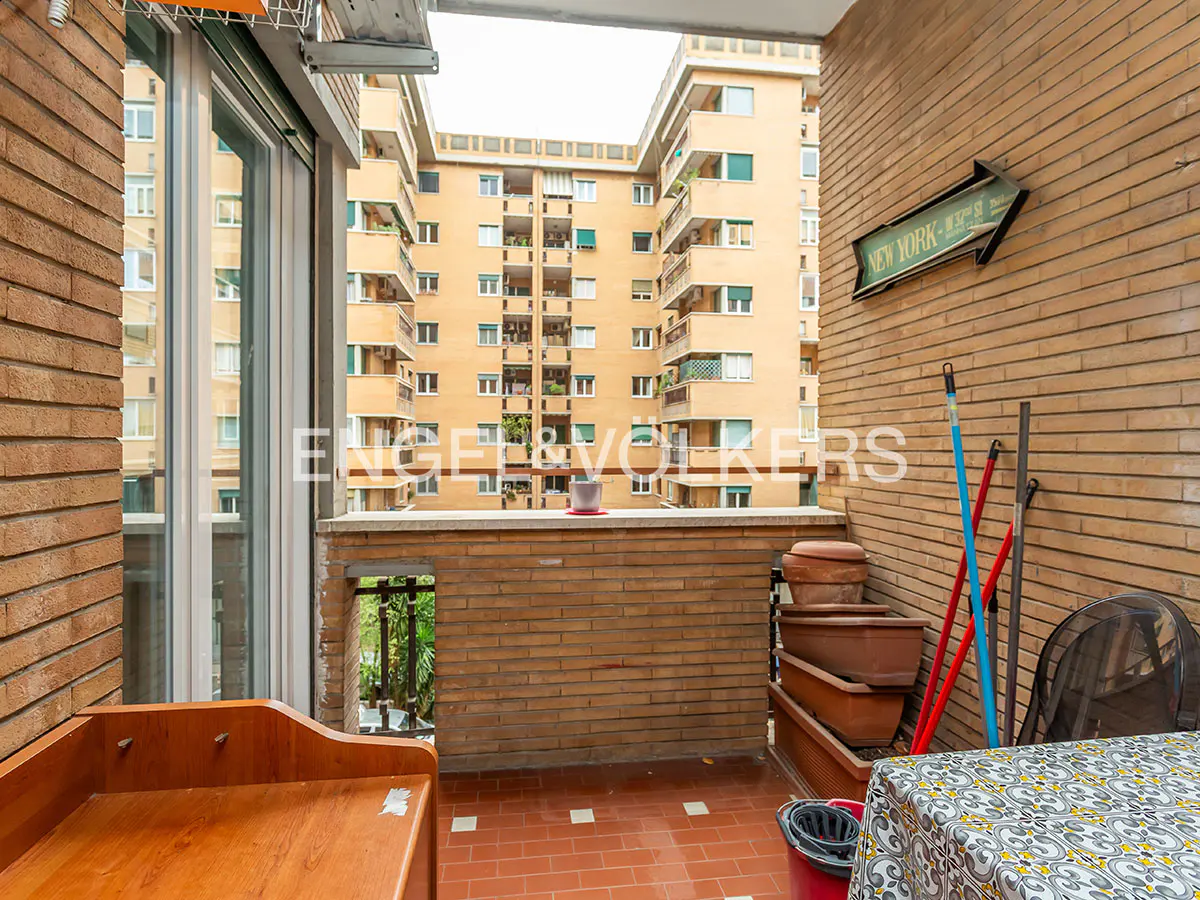 Balcony view with brick walls, terracotta tile floor, and a view of a yellow apartment building. A New York sign hangs on the wall.