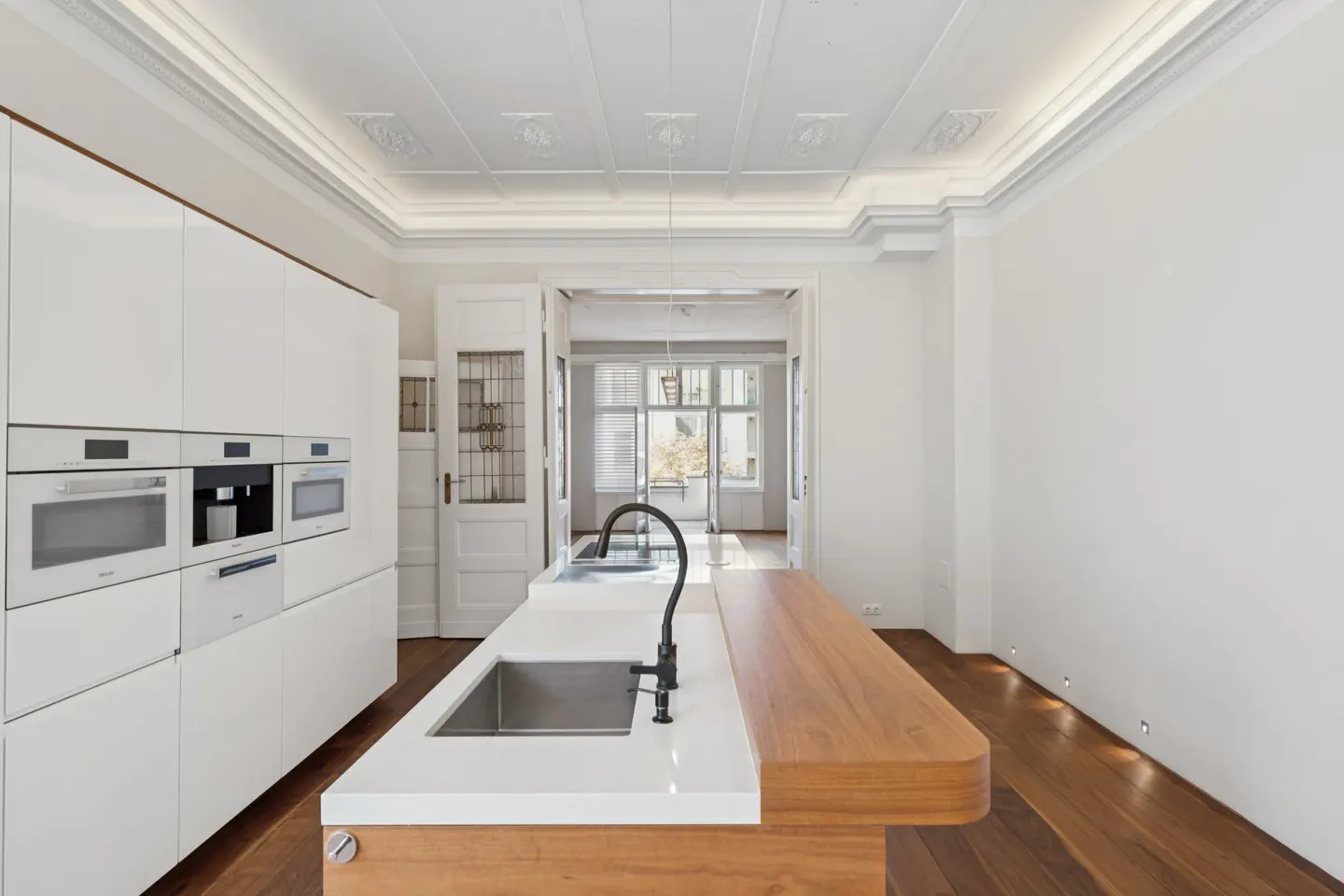 Bright kitchen with white cabinets, stainless steel sink, and wood island. Ornate ceiling and hardwood floors add character.