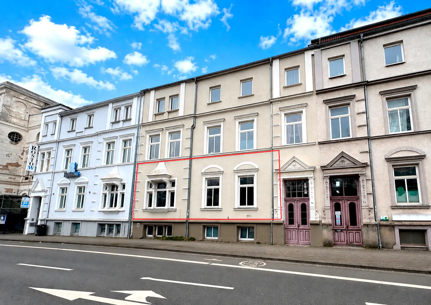Row of townhouses with a beige one outlined in red. The sky is blue with white clouds.