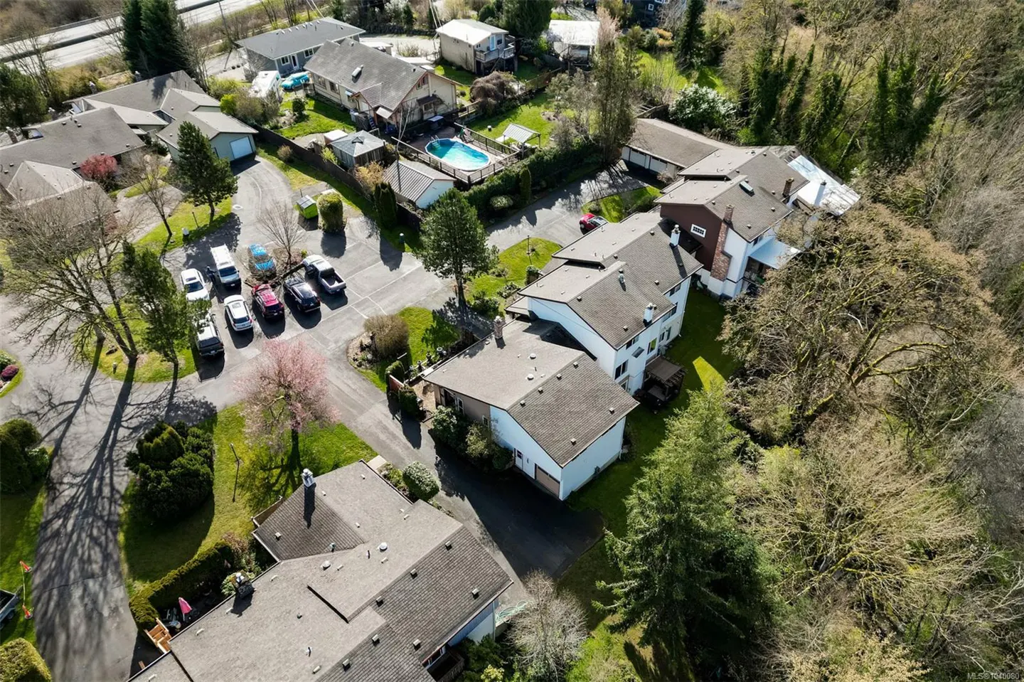 Aerial view of a residential neighborhood with houses, a parking area with several cars, and a backyard swimming pool.