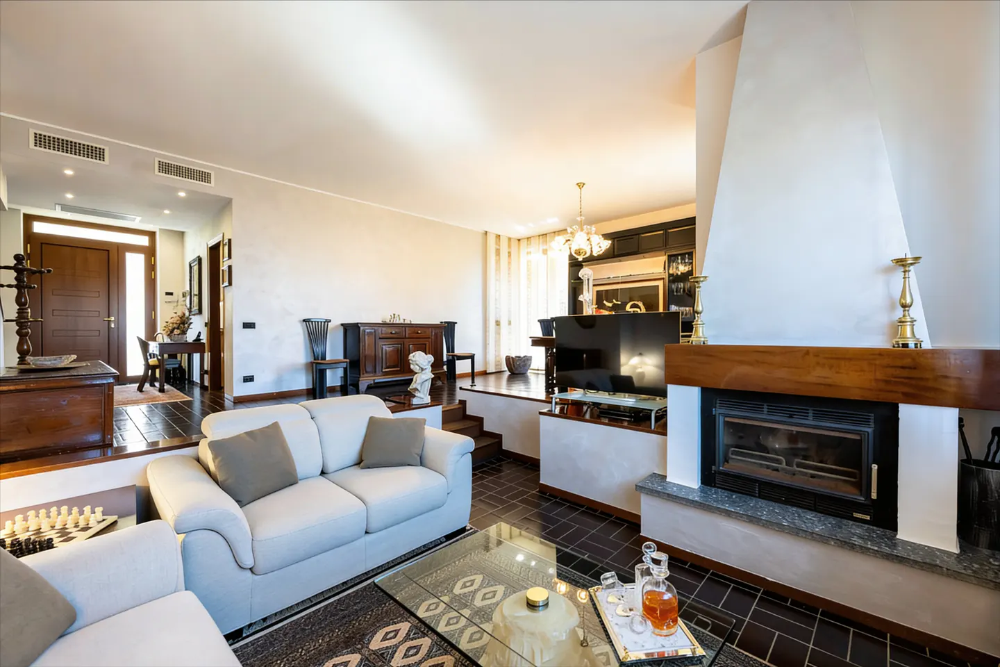 A bright living room with a white sofa, fireplace, and glass coffee table. Dark wood floors and furniture add contrast.