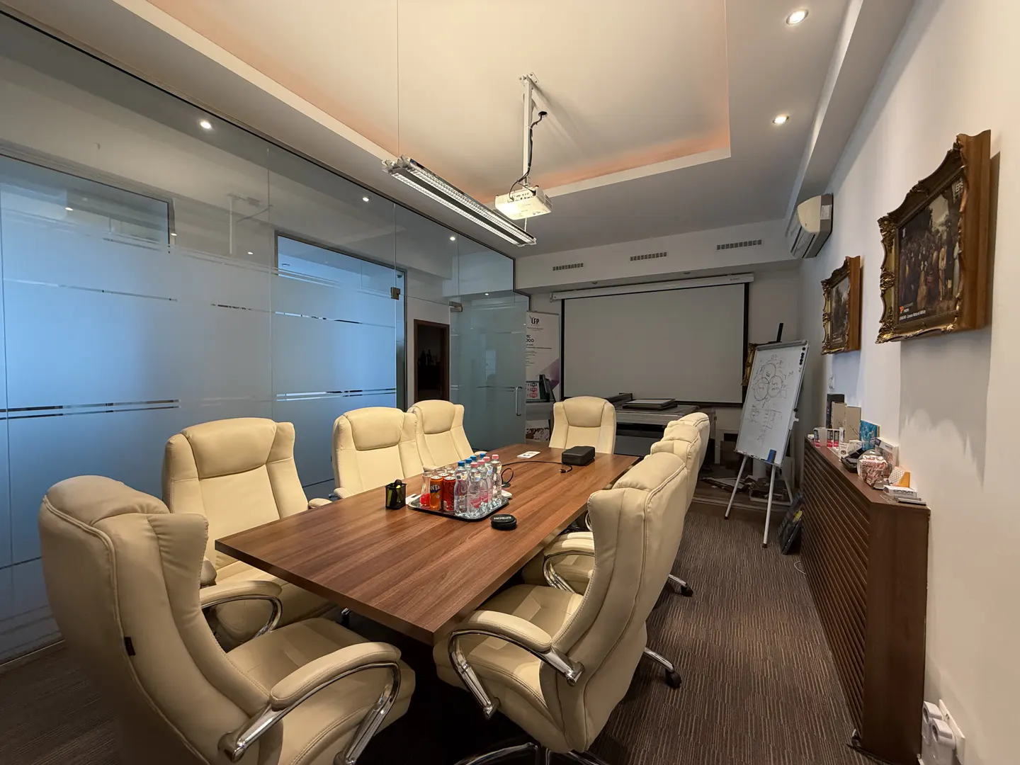 Conference room with a wood table, beige leather chairs, projector, and frosted glass walls.