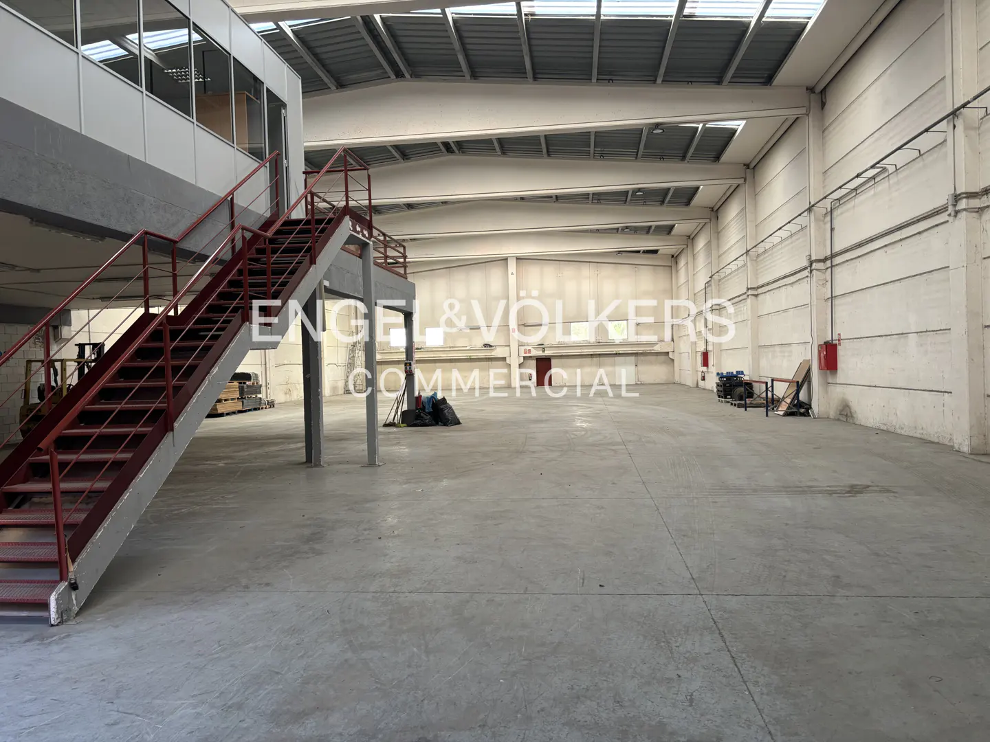 A large, empty warehouse with a red staircase leading to an office area.
