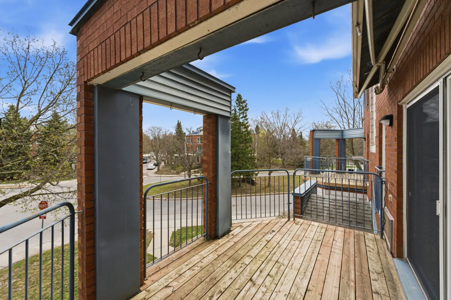 View from a wooden balcony with metal railings, brick columns, and a view of a street with trees.