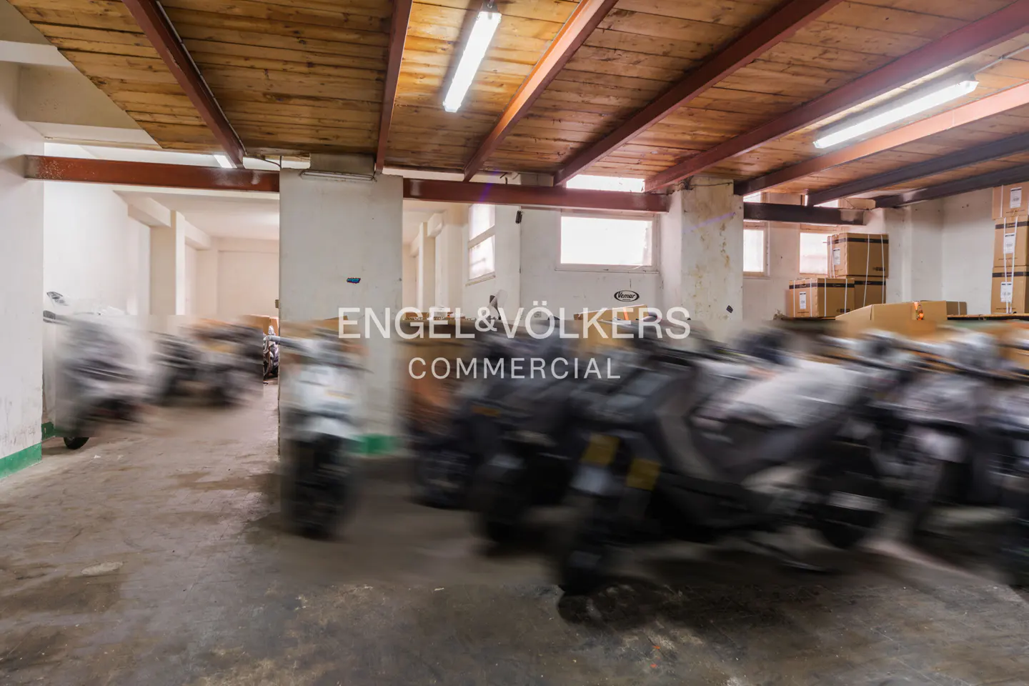 A blurry view of a warehouse with motorcycles, a wooden ceiling, and the Engel & Volkers Commercial logo.