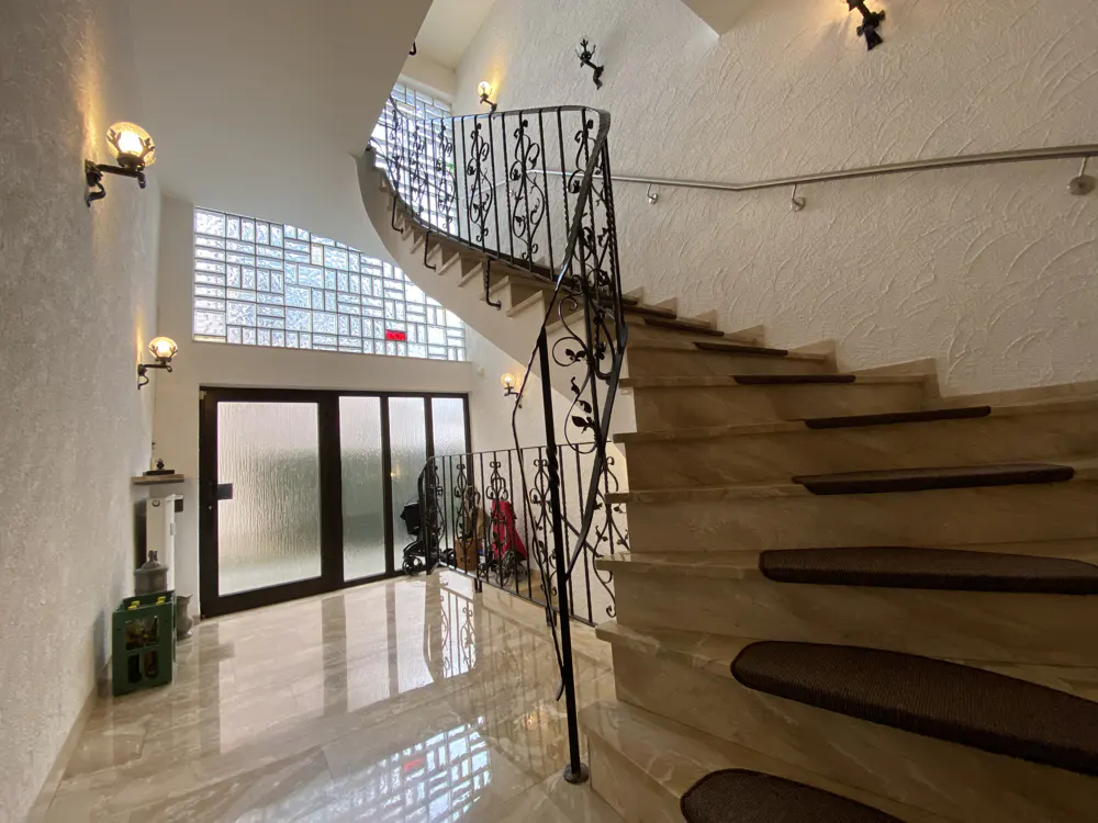 Interior view of a home featuring a curved staircase with a decorative wrought iron railing and marble steps with brown treads. A glass block window is visible.