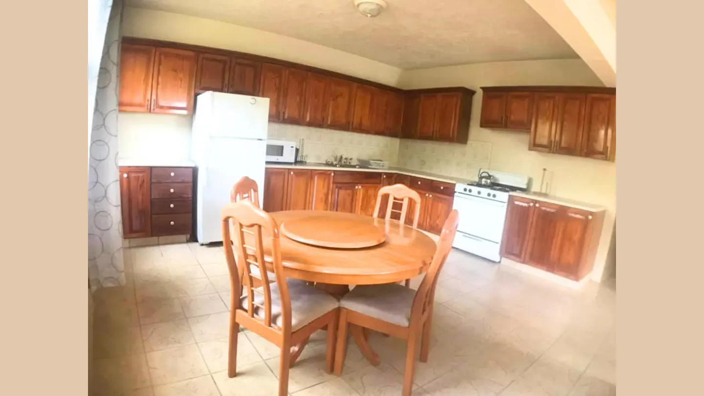 Kitchen with wooden cabinets, white appliances, and a round wooden dining table with four chairs on a tiled floor.