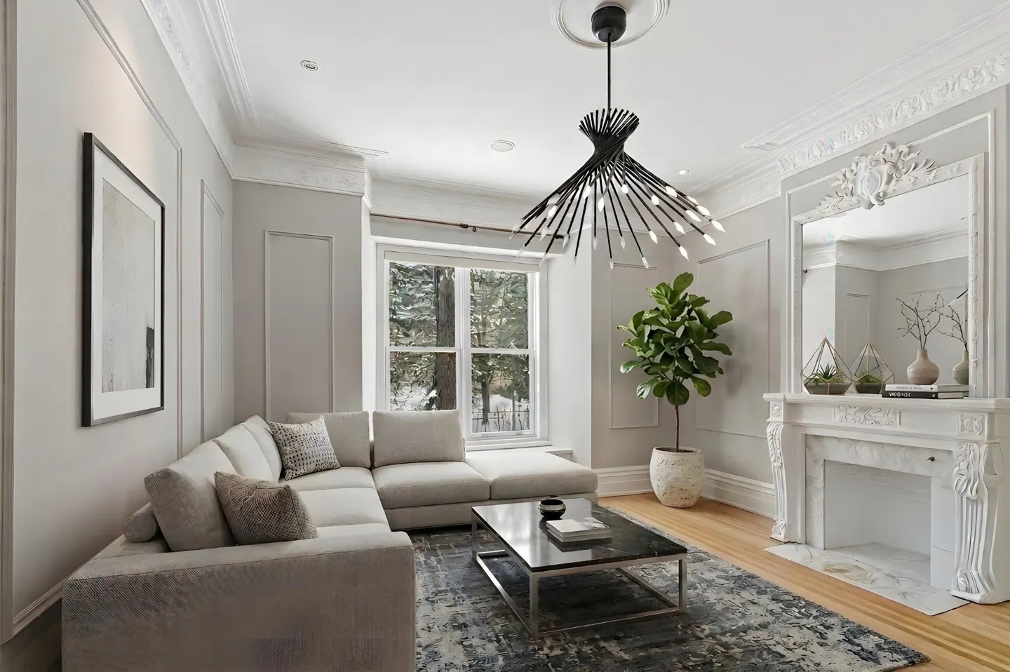 Bright living room with a gray sectional sofa, black marble coffee table, and a modern black chandelier. A white fireplace and a large window are also visible.