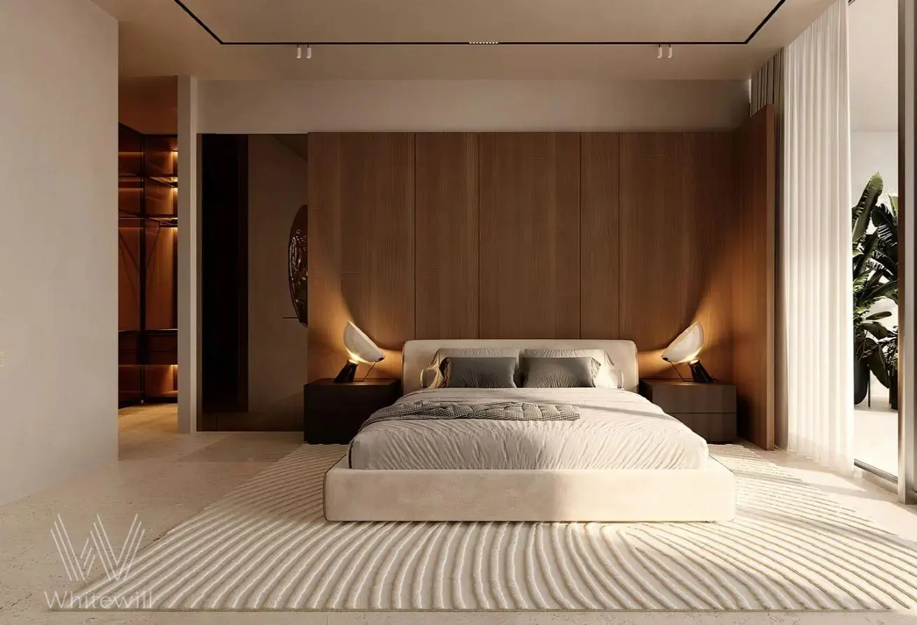 A modern bedroom with a king bed, wood panel headboard, and a textured white rug. Nightstands with lamps flank the bed. A walk-in closet is visible.