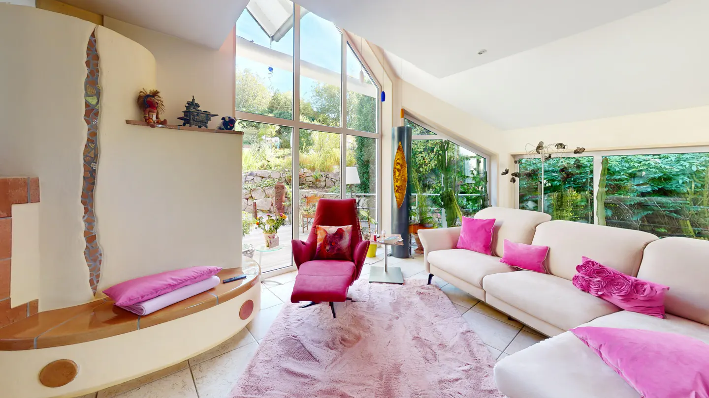 Bright living room with large windows, a pink chaise lounge, and a white sofa with pink pillows. A pink rug covers the tile floor.