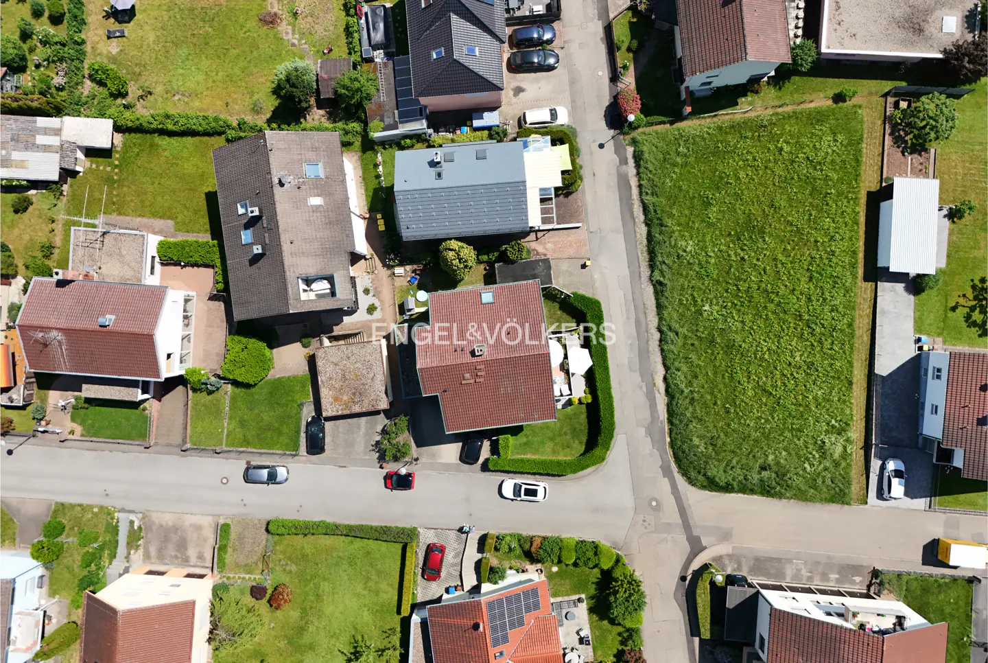 Aerial view of a residential neighborhood with houses, green lawns, and streets with parked cars.