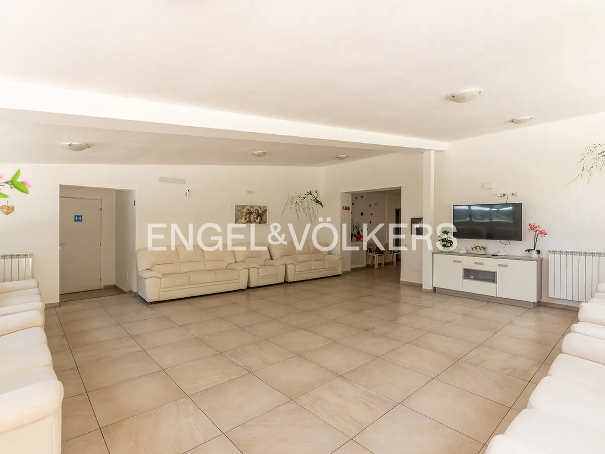 Spacious white living room with tiled floors, large white sectional sofas, a wall-mounted TV, and a white media console.