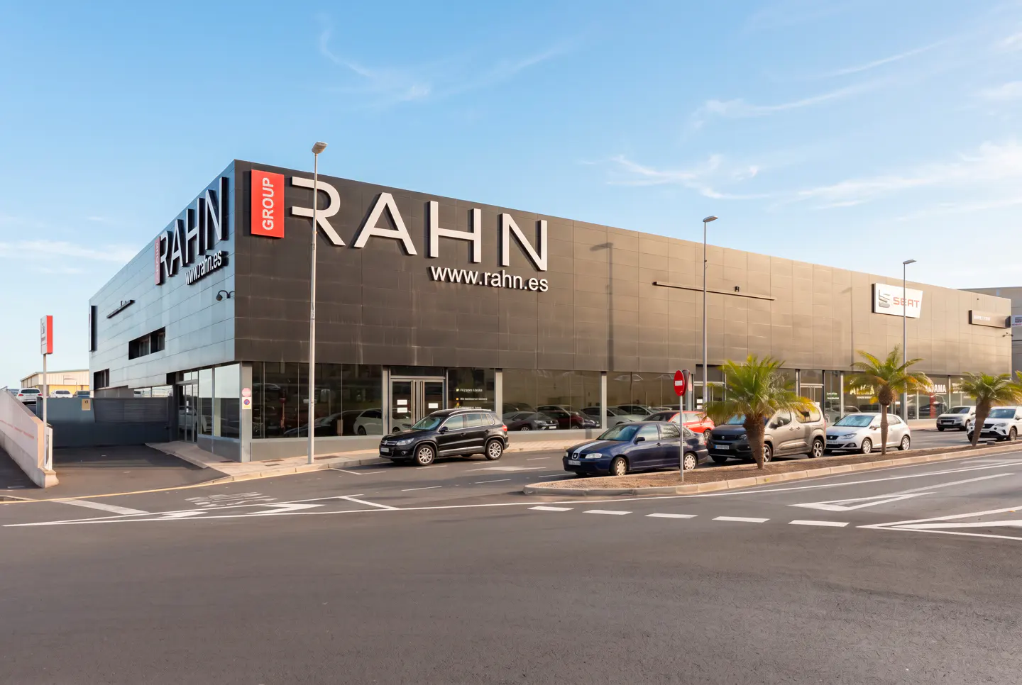 Exterior view of Rahn Group car dealership with parked cars and palm trees under a blue sky.
