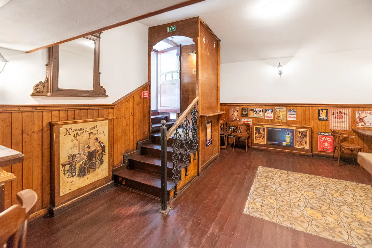 Interior view of a room with wood paneling, stairs with a black iron railing, and vintage posters on the wall.