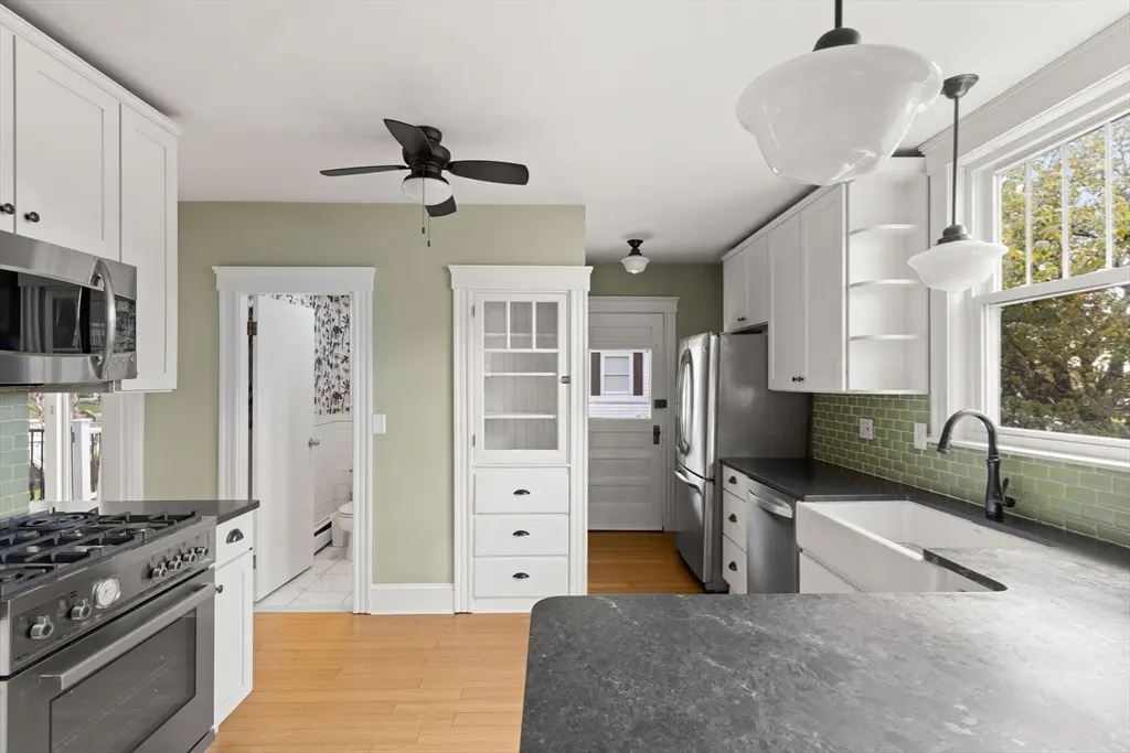 Bright kitchen with white cabinets, stainless steel appliances, and a dark countertop. A window overlooks trees outside.