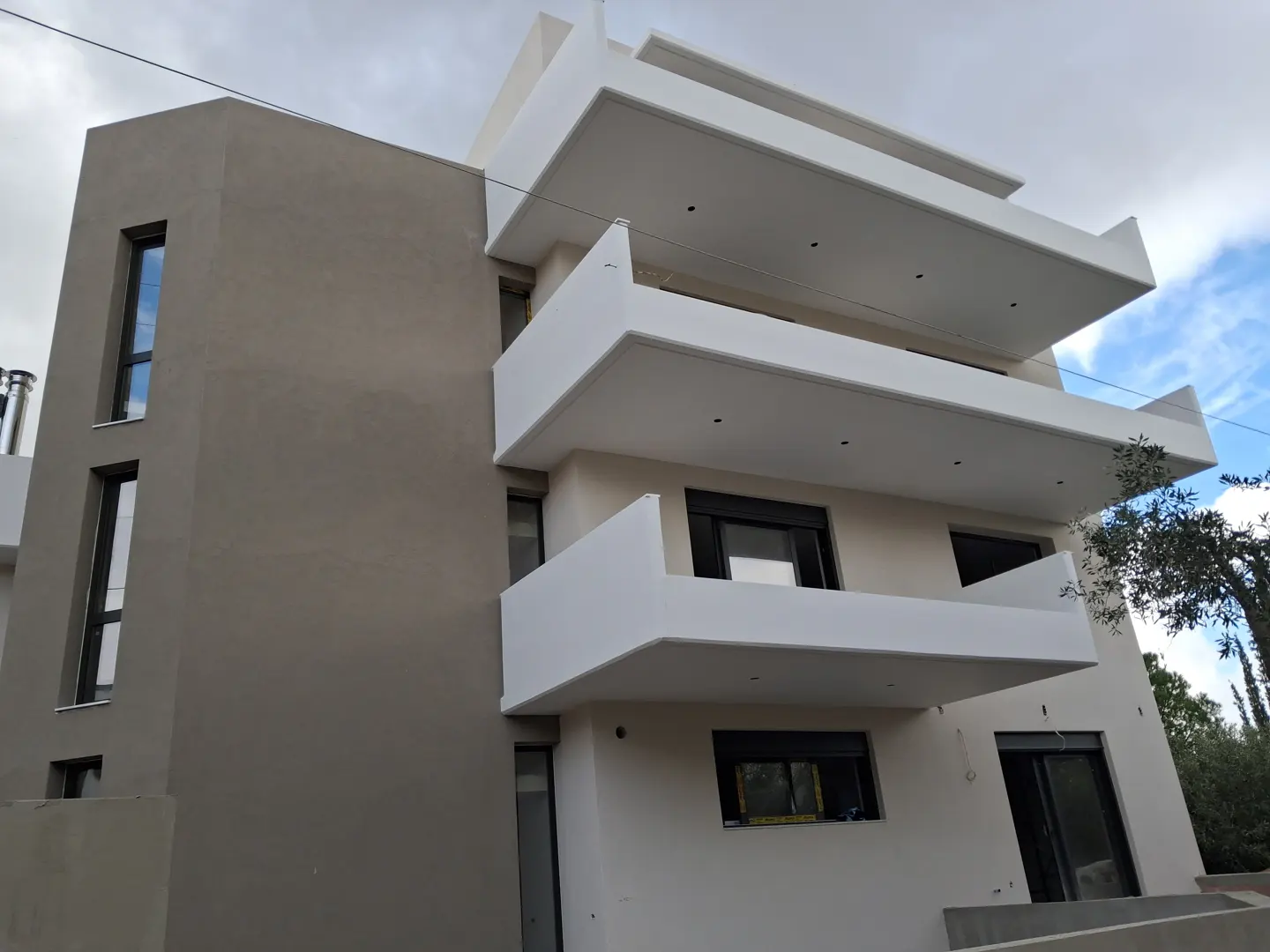 Modern multi-story apartment building with a beige and white facade, featuring stacked balconies and dark window frames.