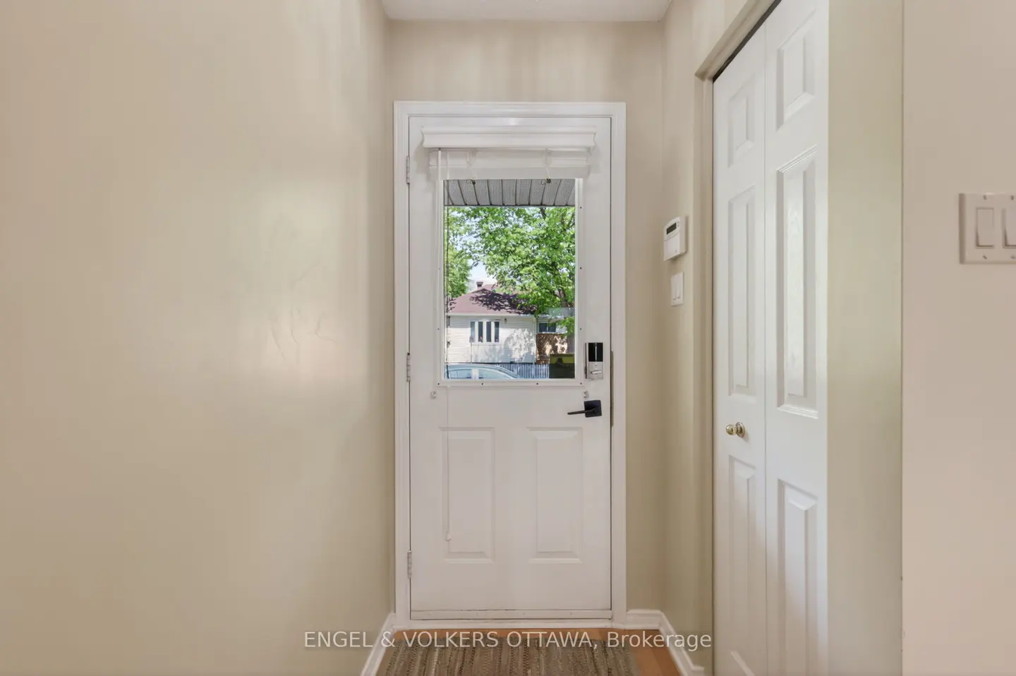 Interior view of a foyer with beige walls, a white door with a window showing a house, and a white closet door.