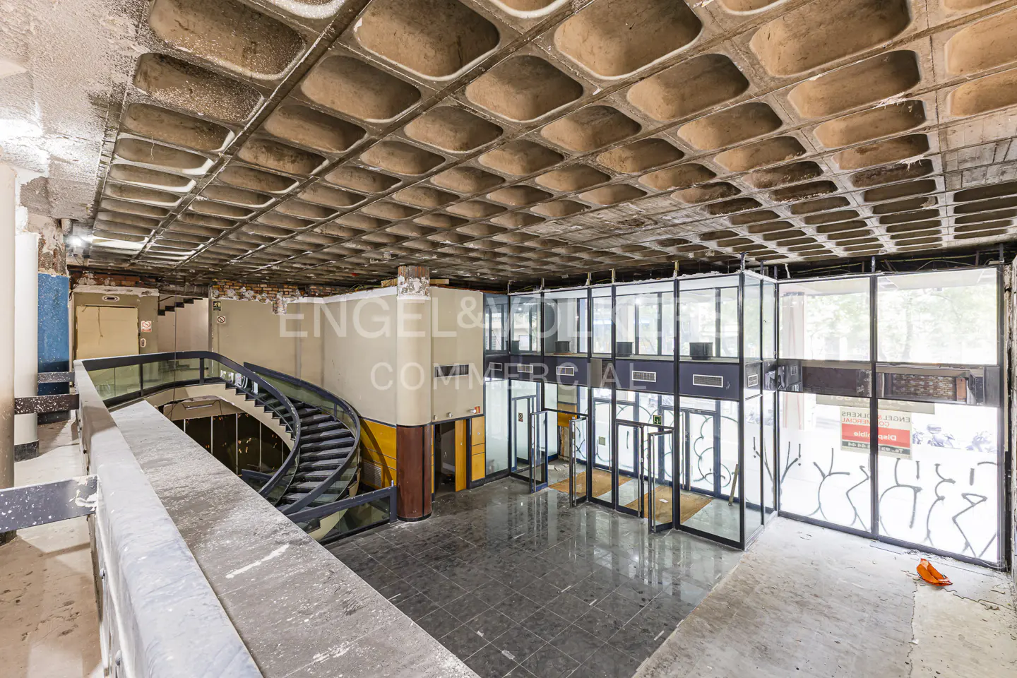 Interior view of a commercial space with a spiral staircase, glass-walled offices, and a coffered ceiling.