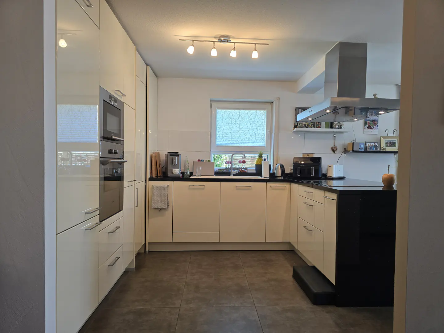 A modern kitchen with cream cabinets, black countertops, and stainless steel appliances. A window provides natural light.