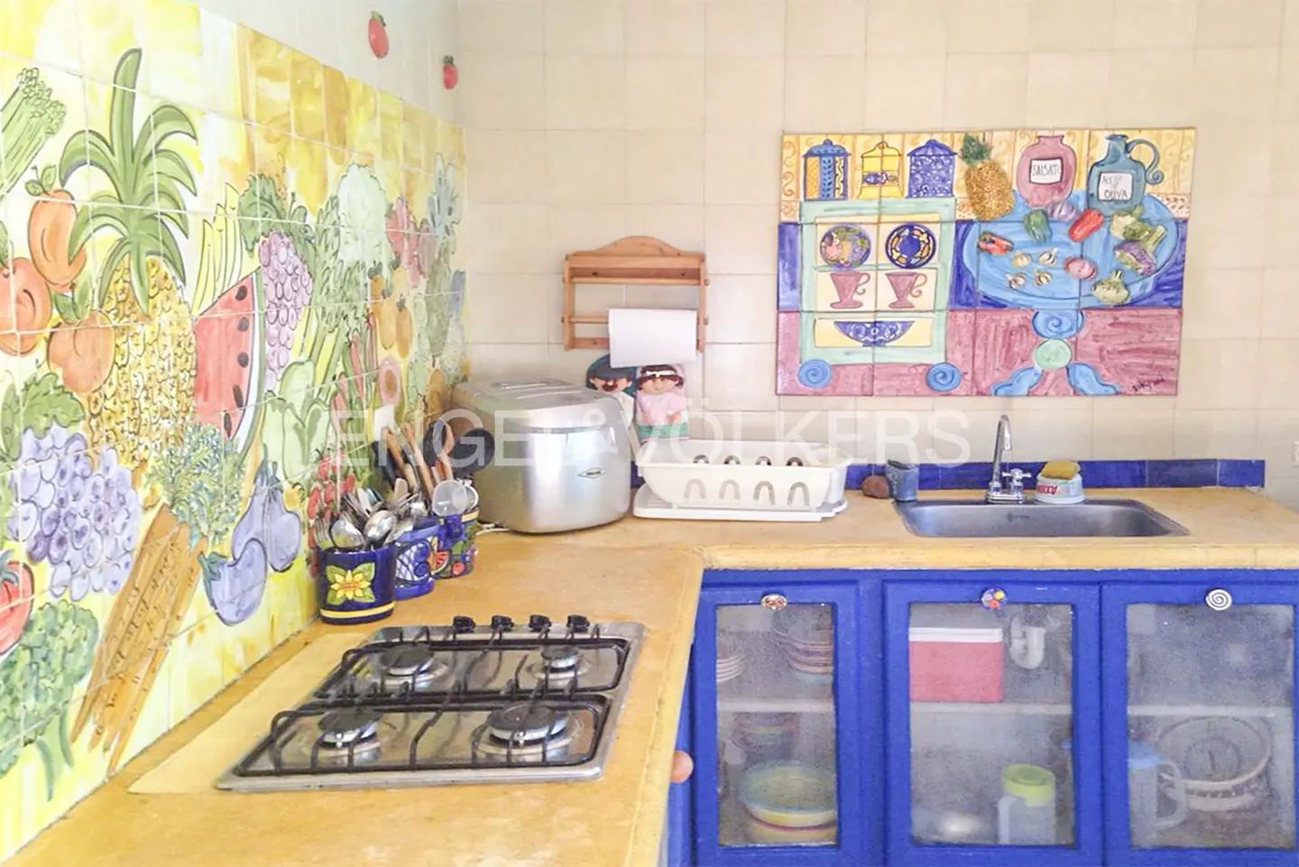 A kitchen with colorful tile art, a stainless steel stove, and blue cabinets.