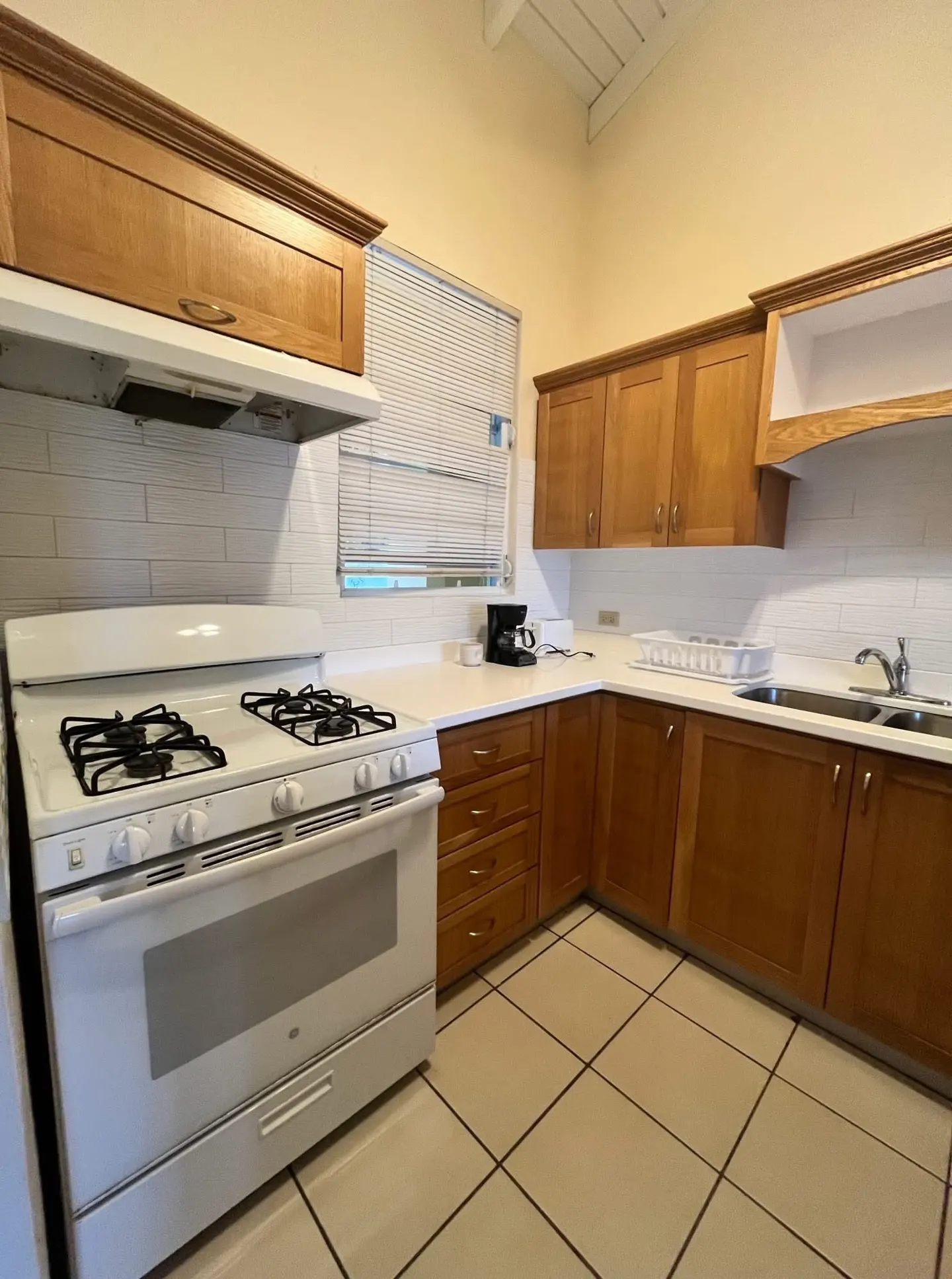A kitchen with light brown cabinets, white countertops, and a white gas stove. The floor is tiled in a light beige color.