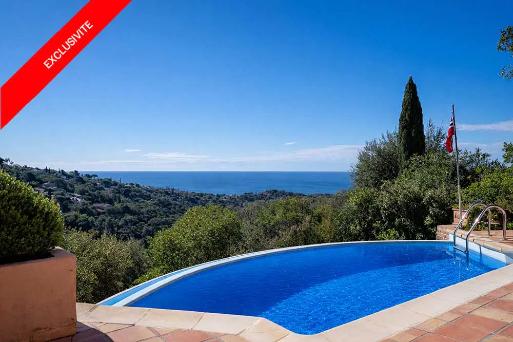 A blue swimming pool with a view of the ocean and green trees under a blue sky. "Exclusivite" red banner in the upper left corner.