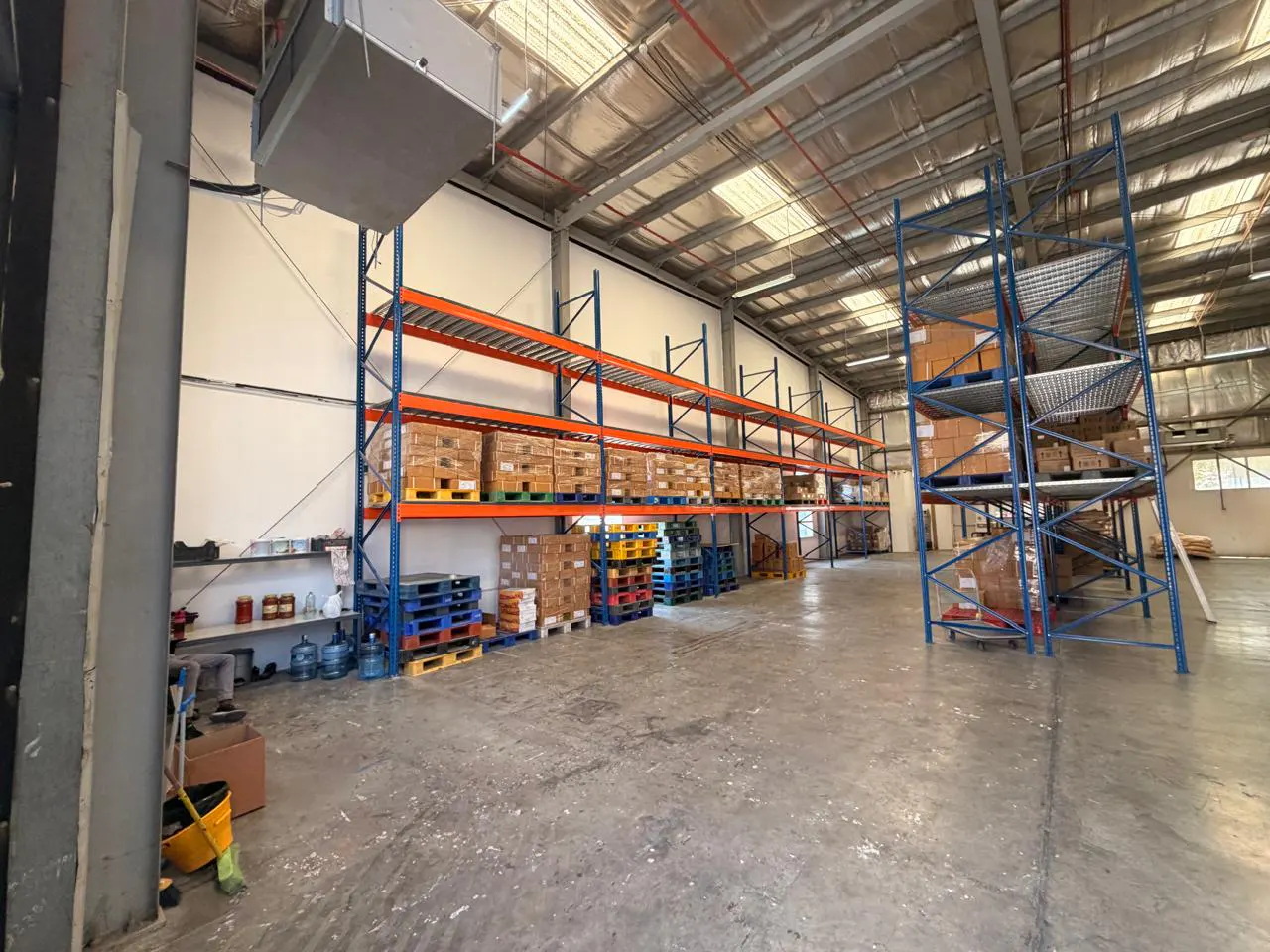 A warehouse interior with tall blue and orange shelves filled with boxes and pallets.