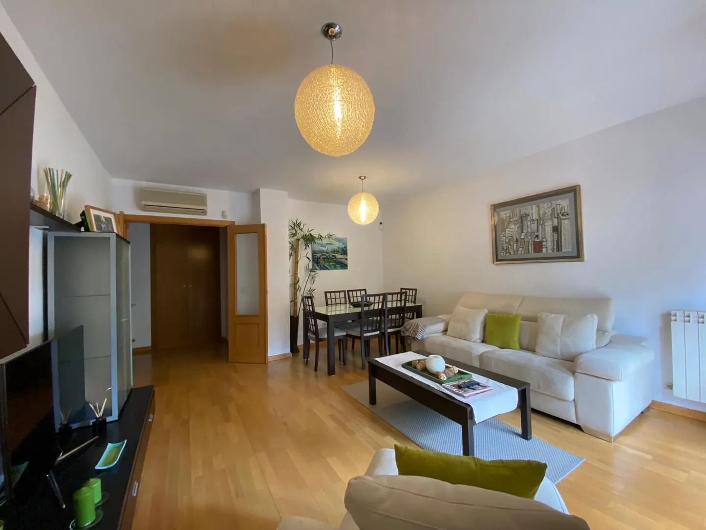 Bright living room with light wood floors, a cream sofa, a dark wood dining set, and two spherical pendant lights.