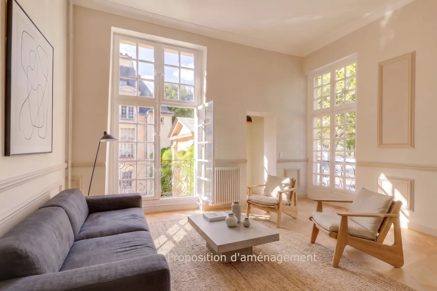 Bright living room with a grey sofa, two wooden armchairs, a concrete coffee table, and large windows overlooking a city.