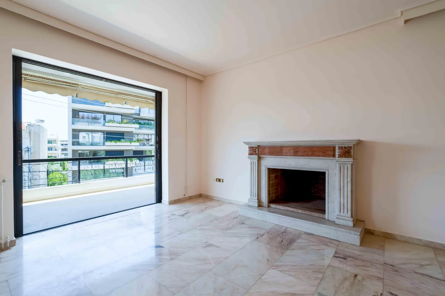 Bright, empty room with marble floors, a fireplace, and a sliding glass door to a balcony.