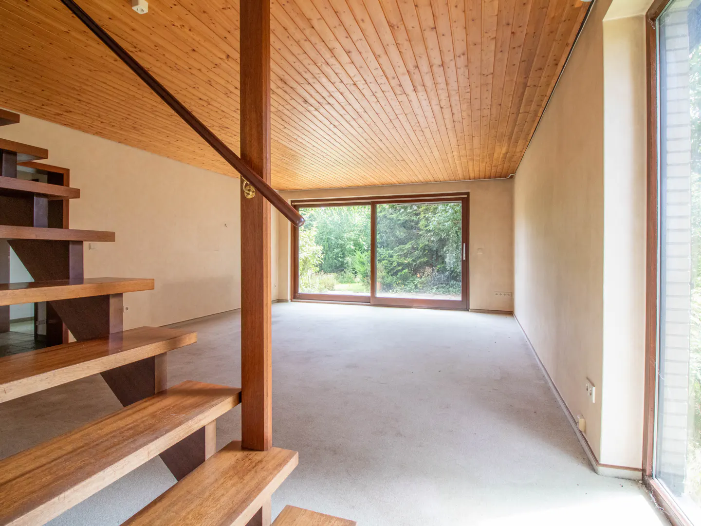 Unfurnished room with wood ceiling, stairs, and large sliding glass doors to a green backyard.