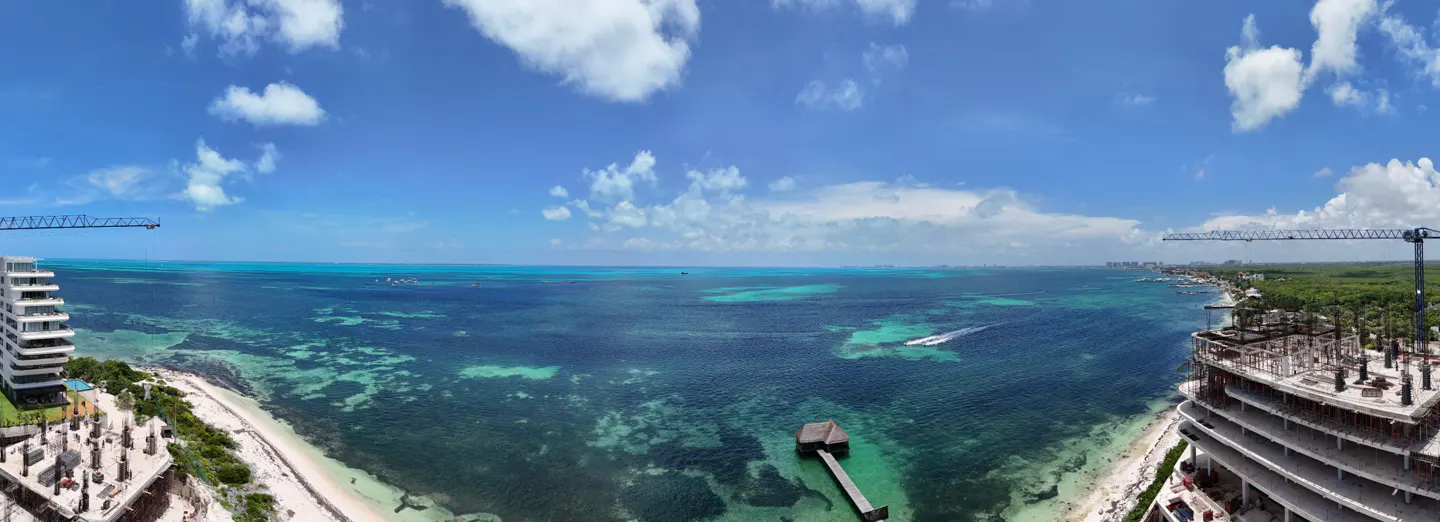 Ocean view from a high-rise under construction, with a pier, beach, and blue sky with white clouds.