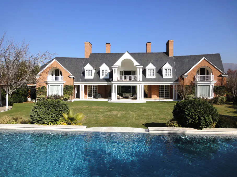 A large brick house with a dark roof, white trim, and a blue swimming pool in the foreground.
