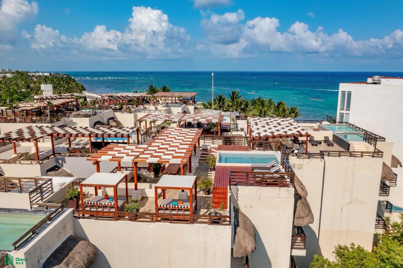 High-angle view of a resort rooftop with wooden pergolas, lounge beds, and small pools overlooking the turquoise ocean. [AI-generated text]