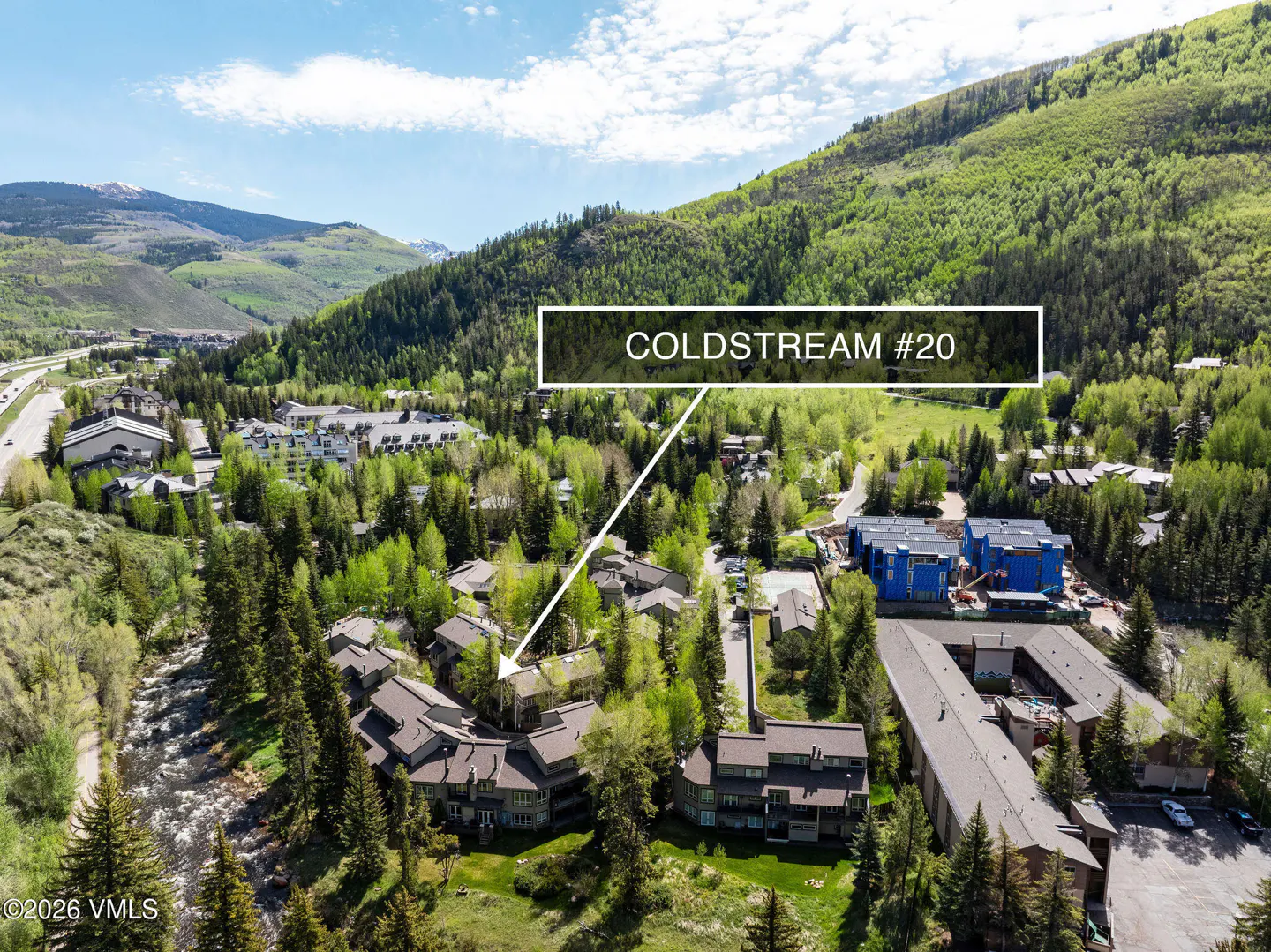 Aerial view of Coldstream #20, a multi-story brown building surrounded by green trees, with mountains in the background.