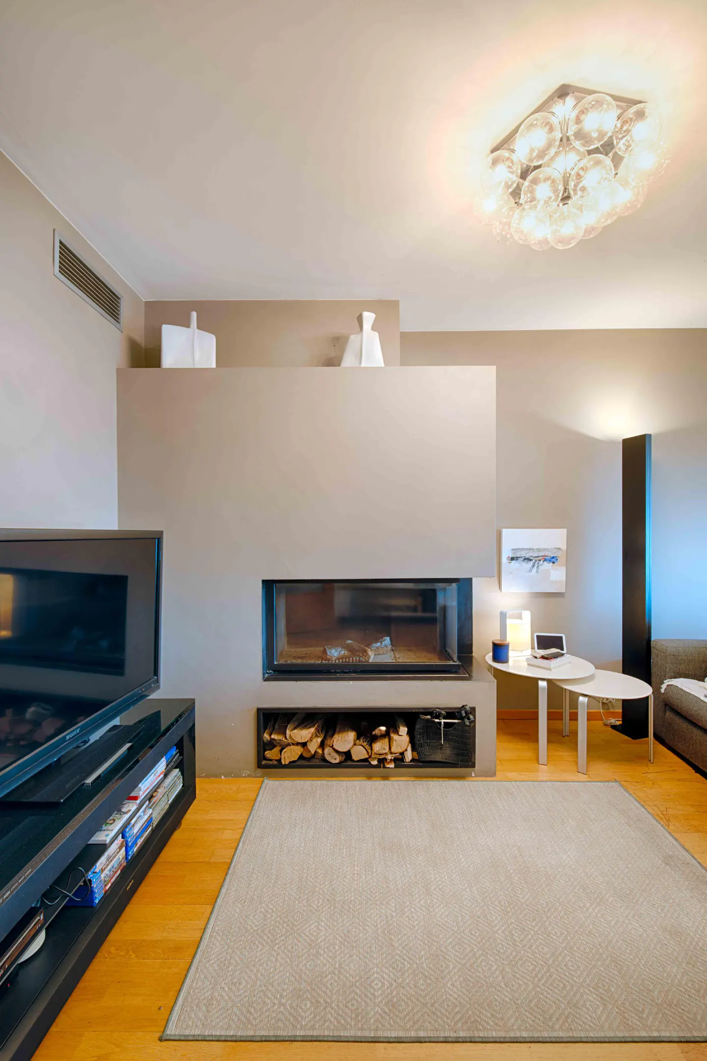 Living room with a modern fireplace, light gray rug, and wood floors. A TV and table are visible.