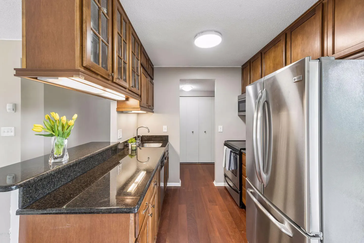 A kitchen with wood cabinets, black granite countertops, stainless steel appliances, and wood floors.