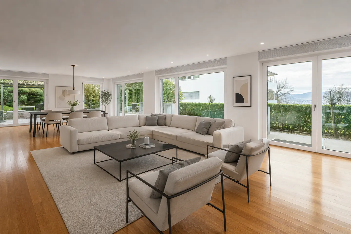 Modern living room with a large beige sectional, two armchairs, a black coffee table, and floor-to-ceiling glass doors.