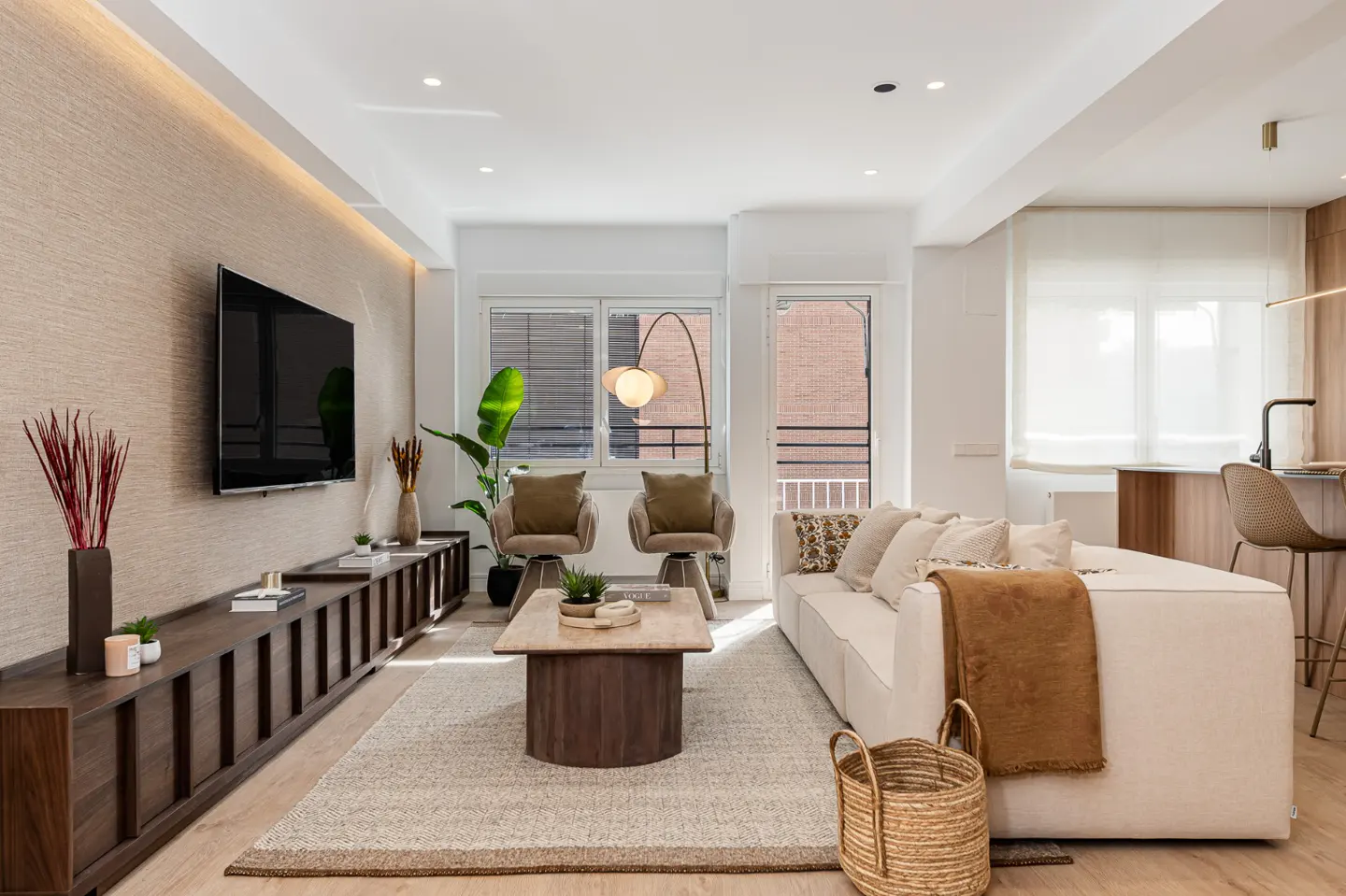 Bright living room with a white sofa, wooden furniture, a TV, and a large window. A woven basket sits on the floor.