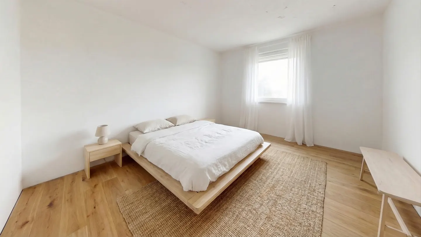 Minimalist bedroom with white walls, light wood floors, and a platform bed with white linens. A jute rug sits beneath the bed.