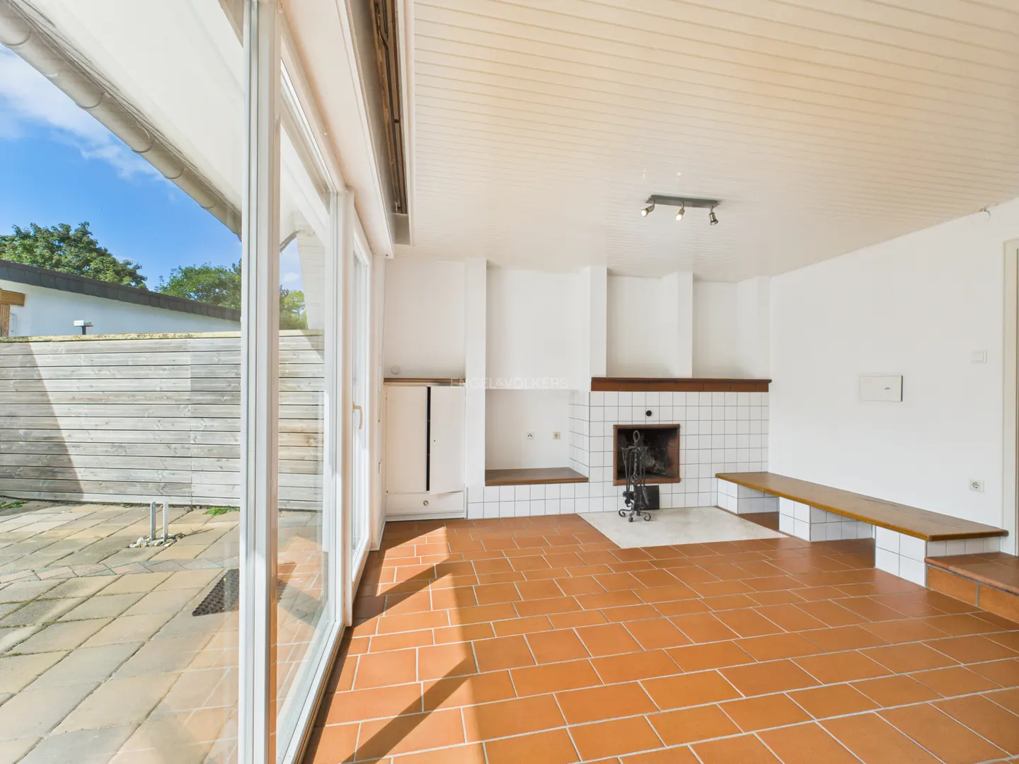 Bright living room with terracotta tile floor, white walls, and a tiled fireplace. Sliding glass doors lead to a patio.