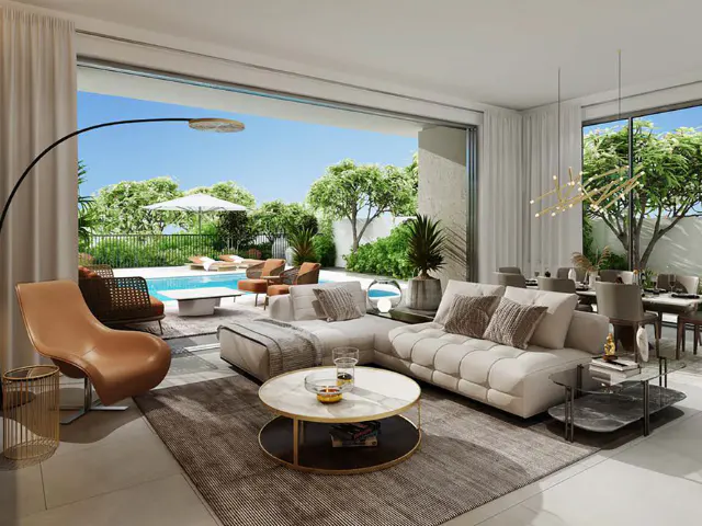 Bright, modern living room with a beige sectional sofa, round coffee table, and floor lamp. Outside, a pool and patio furniture are visible.