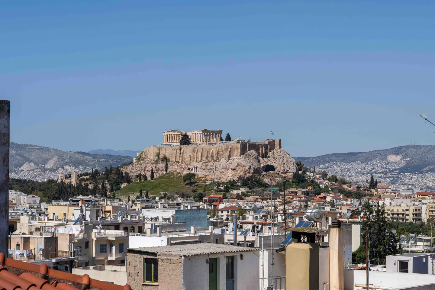 Athens cityscape view with the Acropolis on a hill in the background under a clear blue sky.