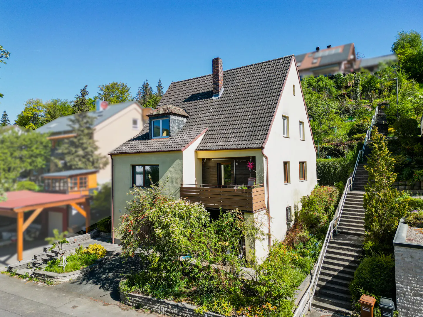 Two-story house with a balcony, a gray tile roof, and a brick chimney, surrounded by greenery and a long staircase.