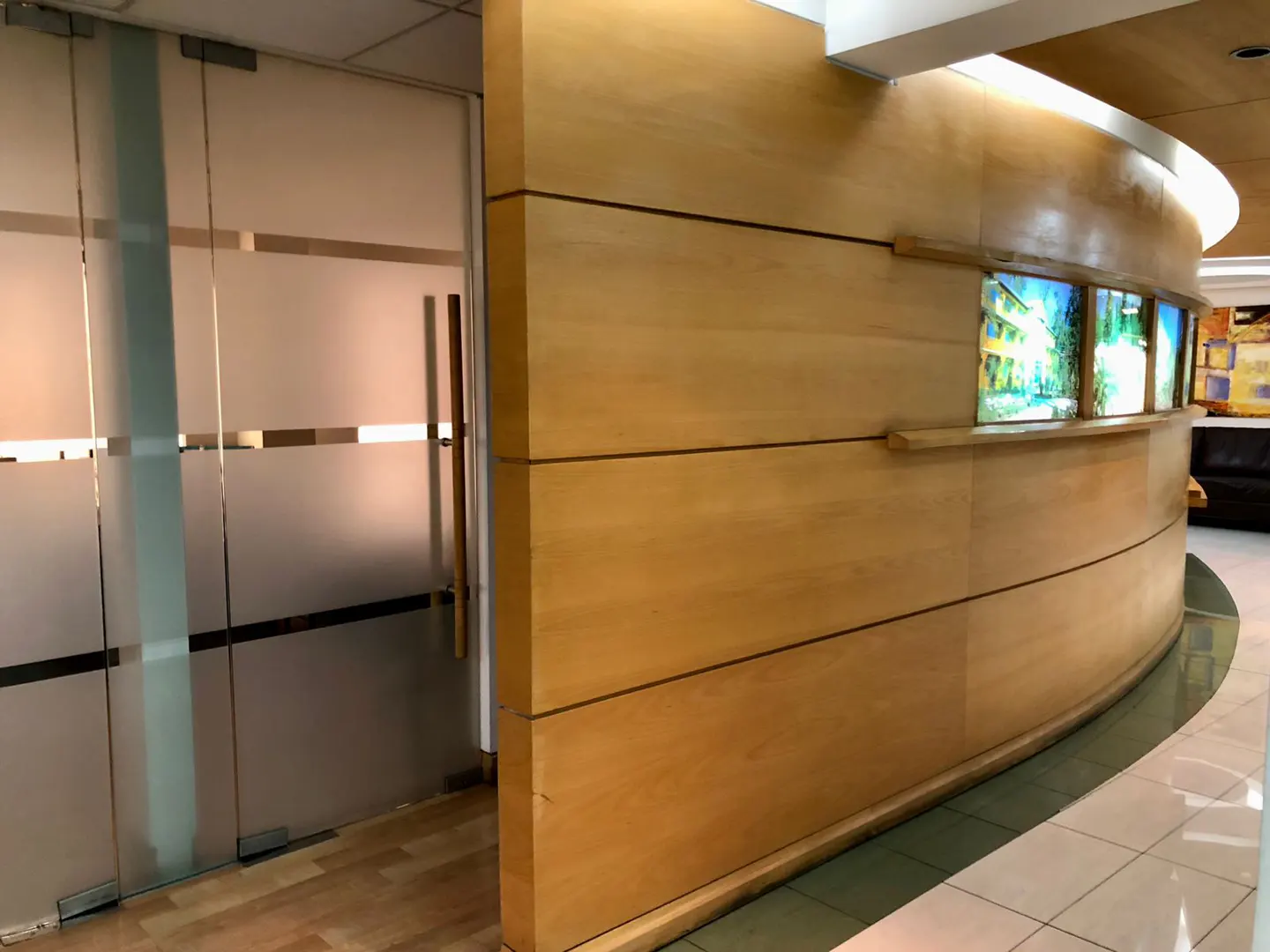 Office interior with frosted glass doors and a curved wooden wall featuring landscape art.