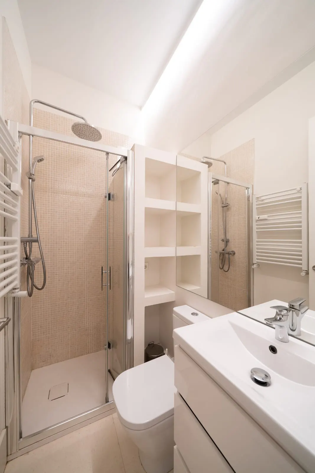 Bright bathroom with a glass-enclosed shower, white toilet, sink vanity, and built-in shelving.