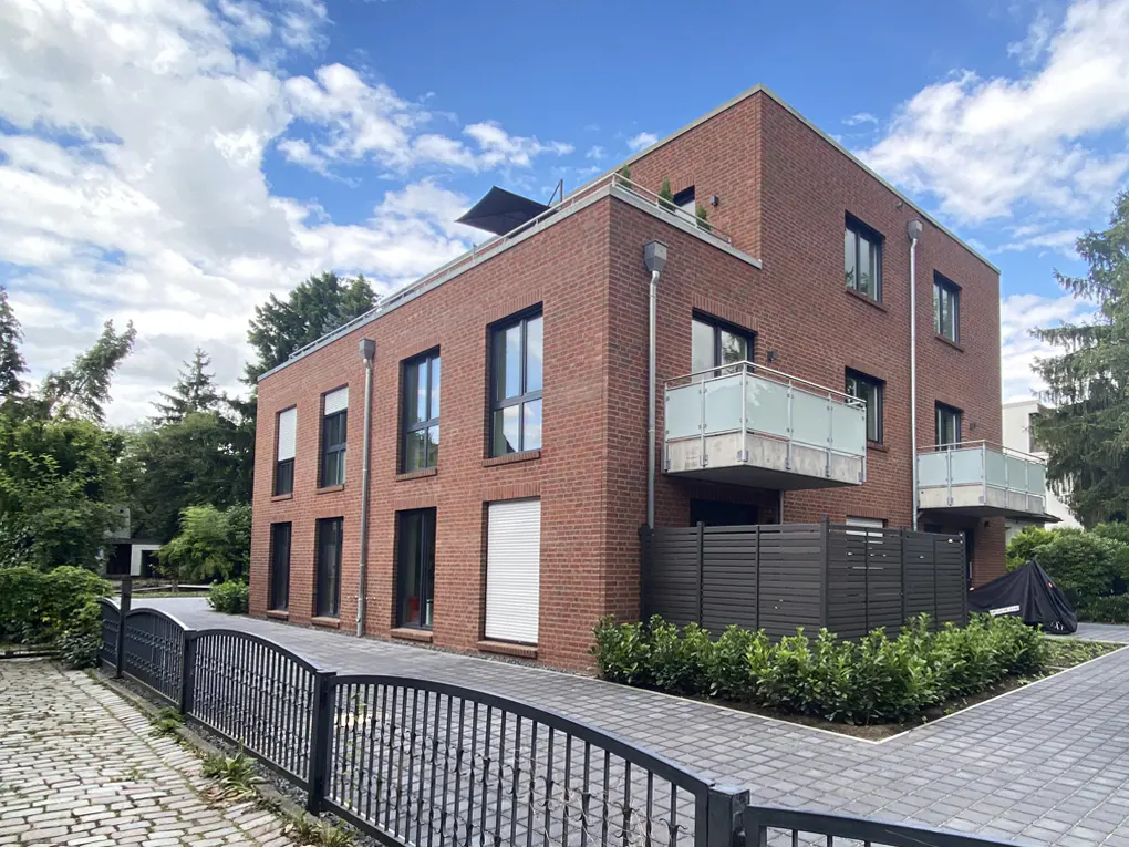 A modern, two-story brick building with balconies, black framed windows, and a black metal fence in front.